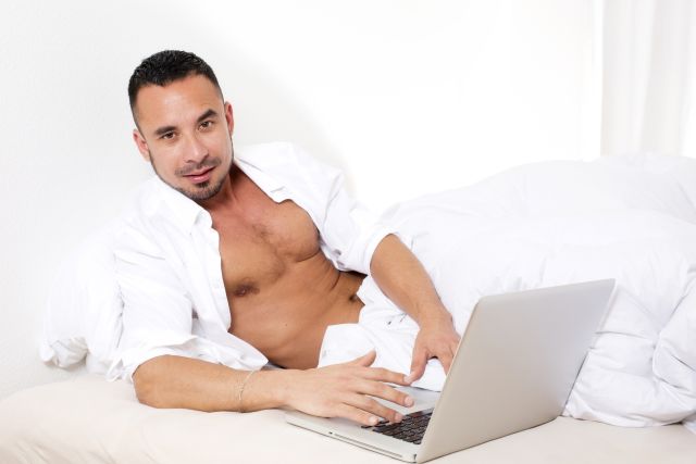 Mit der richtigen Strategie zum perfekten Flirt Attraktiver Mann mit Laptop im Bett